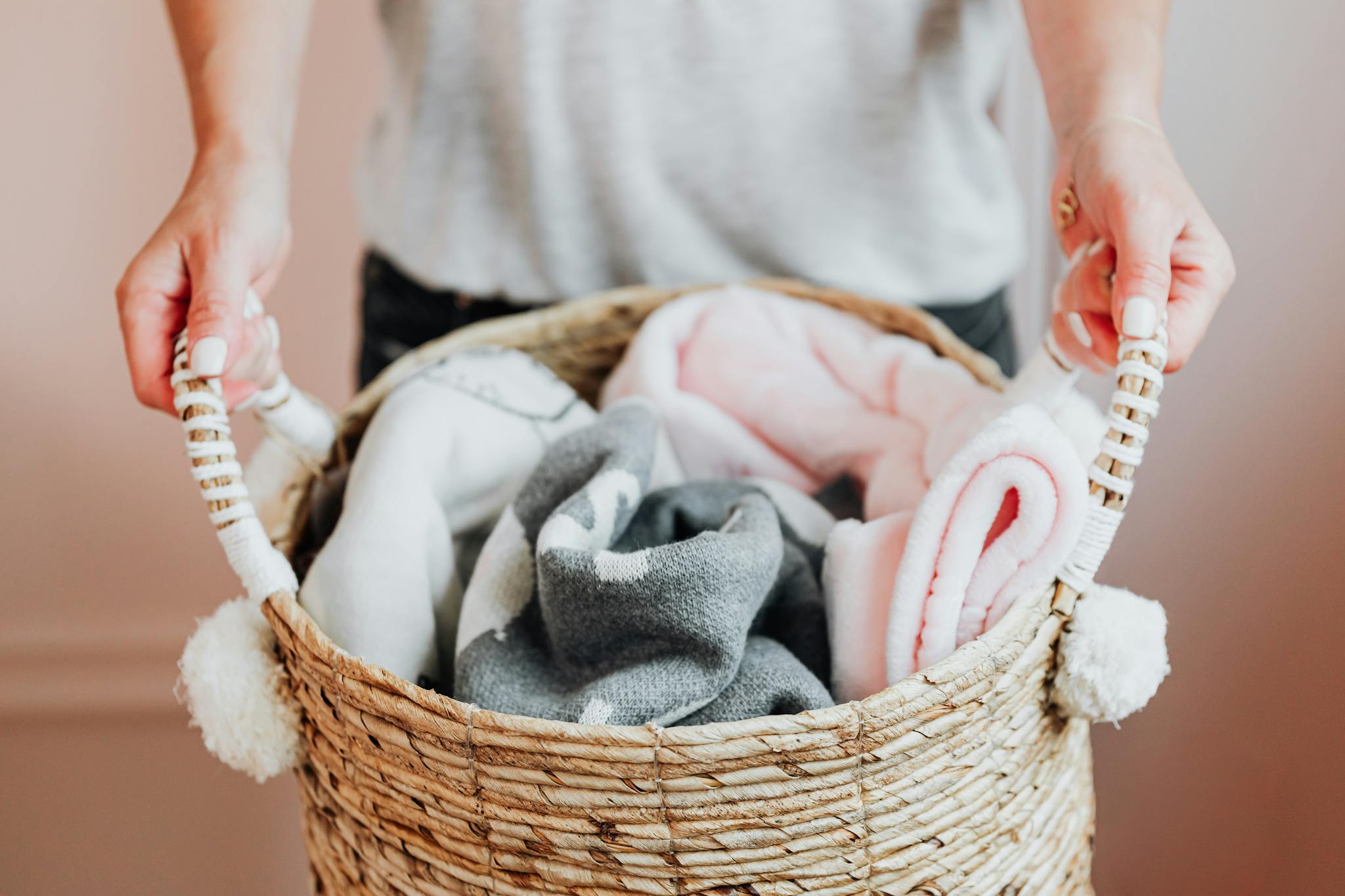 Close-up of hands holding a woven basket full of soft baby blankets indoors.